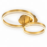 Modern ceiling light fixture with two interlocking circular rings in brushed gold, emitting a warm white glow against a plain white background.