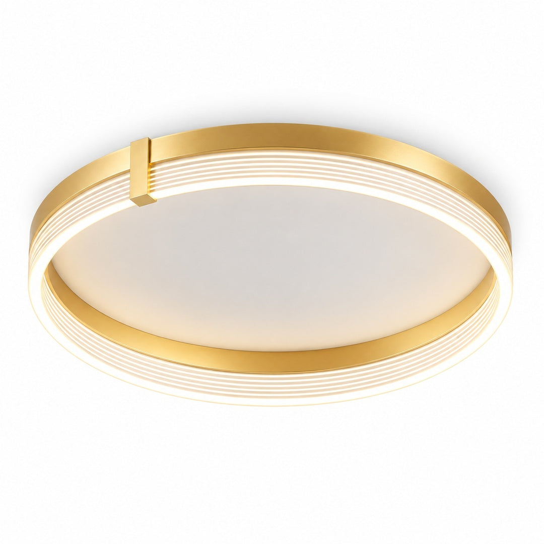 A modern flush-mount ceiling light fixture with a circular design, featuring a brushed gold metal frame with concentric ridges and a warm white frosted center panel.
