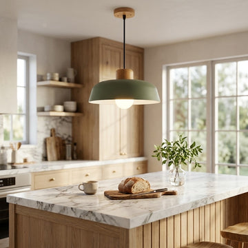 A modern pendant light with a sage green dome shade and a light wood top, hanging over a marble-topped kitchen island in a bright, contemporary kitchen.