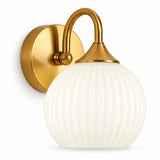 A wall-mounted sconce light fixture with a round white ribbed glass shade and a brushed gold metal wall plate and curved arm, shown against a plain white background.