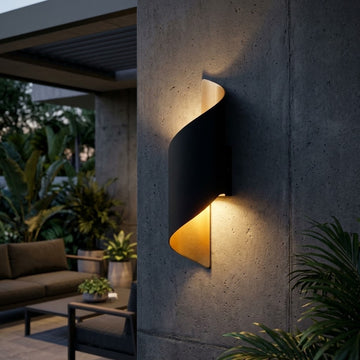 A modern spiral-shaped wall sconce light fixture mounted on a concrete pillar, casting a warm golden glow downward and upward in an outdoor patio setting.