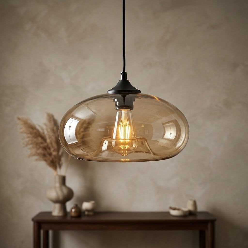A modern pendant light with a translucent amber-tinted glass dome and a black ceiling mount, hanging in a styled room above a dark wood console table.