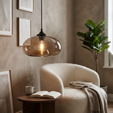 A modern pendant light with a translucent amber-tinted glass dome and a black ceiling mount, hanging in a cozy living room above a cream bouclé armchair.