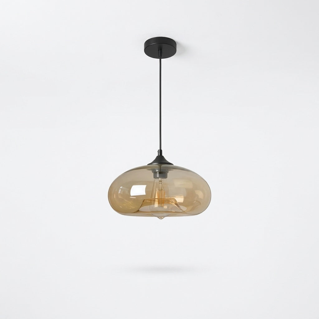 A modern pendant light with a black ceiling canopy and cord, featuring a translucent amber-tinted glass shade that reveals a warm glowing filament bulb inside, set against a clean white background.