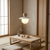 A modern pendant light with a white conical shade and glowing spherical globe bulb hangs over a low wooden table in a minimalist Japanese-style room with tatami flooring, shoji screens, and a tea set.