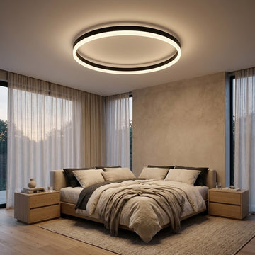 A modern circular LED ceiling light with a black outer ring and glowing white inner ring, installed in a contemporary beige bedroom with a bed, nightstands, and sheer curtains.