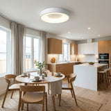 Round white flush mount ceiling light with a glowing ring above a dining table in an open kitchen with wood cabinetry.