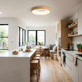 Round wood-look flush mount ceiling light with a glowing ring in a white kitchen with an island and window-side dining nook.