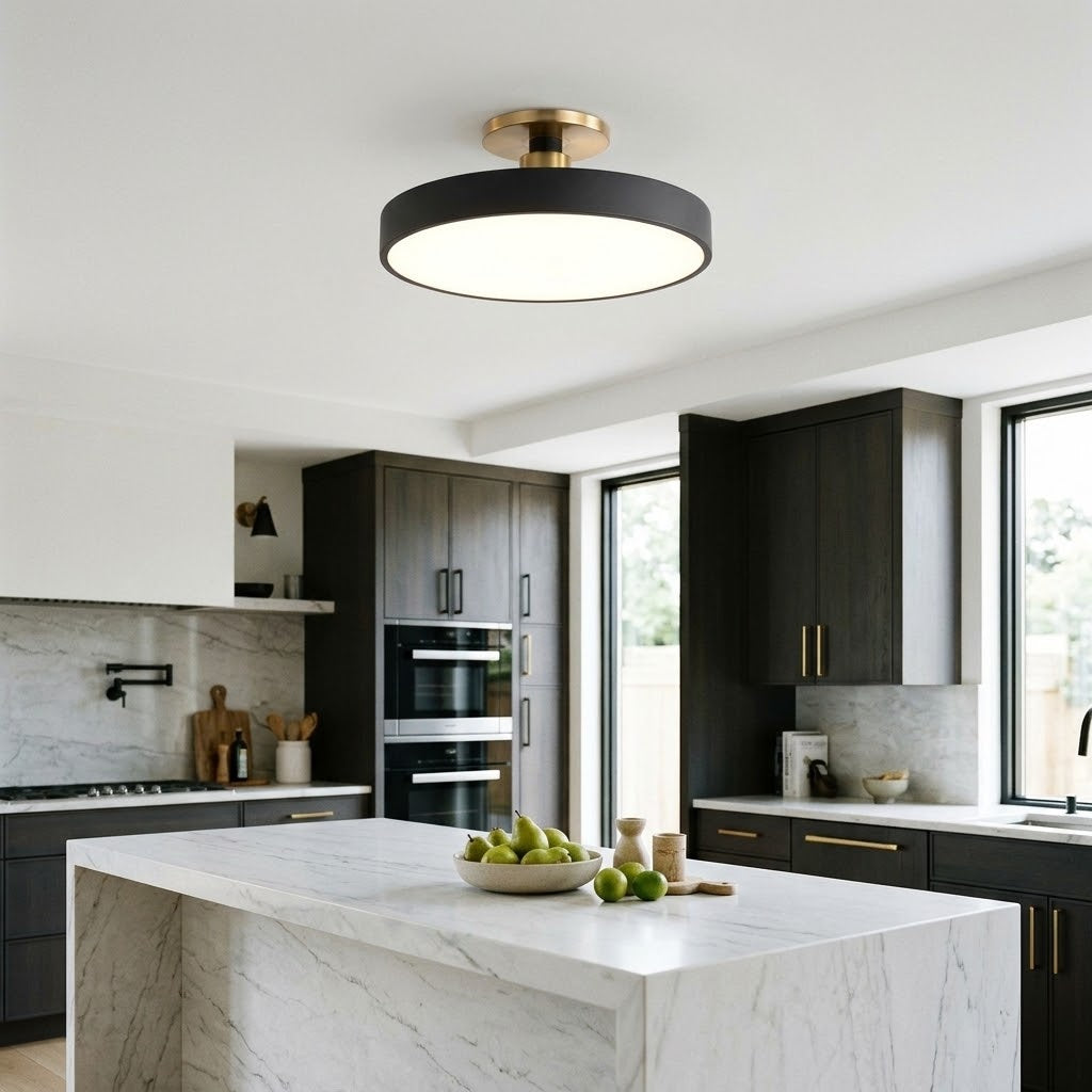 A modern semi-flush mount ceiling light with a black circular frame and a brushed gold ceiling mount, installed in a contemporary kitchen with dark wood cabinets and a white marble island.