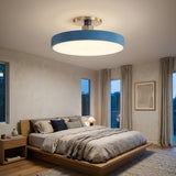 A modern semi-flush mount ceiling light with a blue outer ring and a brushed gold-toned metal cap, installed in a contemporary bedroom with a wooden bed and neutral walls.