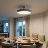 A modern semi-flush mount ceiling light with a circular blue-gray shade and a brushed gold ceiling mount, installed in a bright, contemporary dining room with a wooden table and chairs.