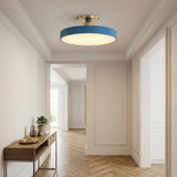 A modern semi-flush mount ceiling light with a blue cylindrical shade and a brushed gold brass ceiling mount, installed in a bright, elegant hallway with cream walls and herringbone wood floors.