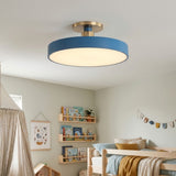 A modern semi-flush mount ceiling light with a matte blue outer ring, a warm white illuminated diffuser, and a brushed gold ceiling canopy, shown installed in a child's bedroom.