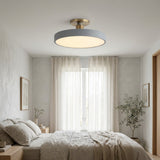 A modern semi-flush mount ceiling light with a circular gray shade and a brushed gold ceiling mount, shown installed in a bright, contemporary bedroom.