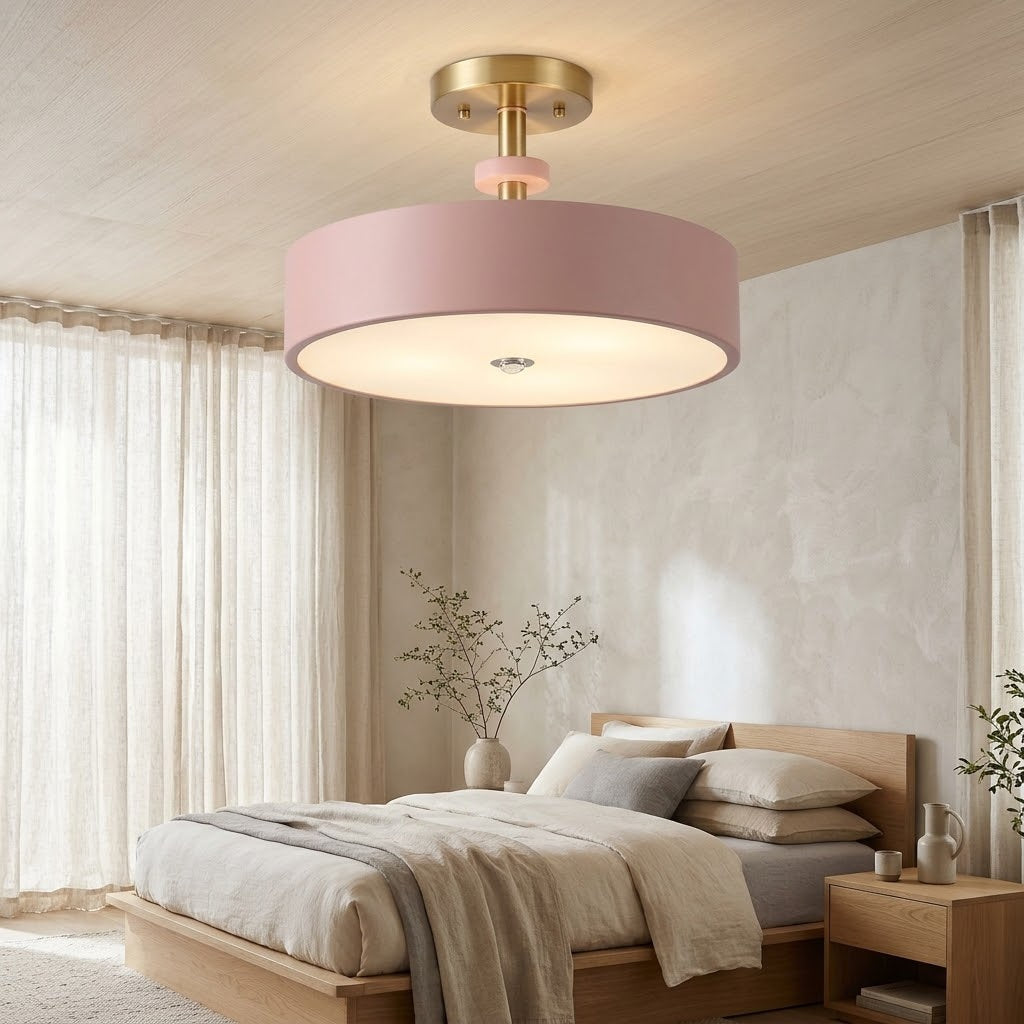 A modern semi-flush mount ceiling light with a wide pink drum shade and a brushed gold ceiling canopy, shown installed in a minimalist, warm-toned bedroom.