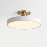 A modern semi-flush mount ceiling light featuring a matte white cylindrical shade and brushed brass metal hardware, shown illuminated against a plain white ceiling.