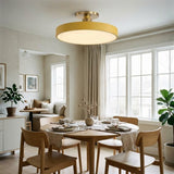 A modern semi-flush mount ceiling light with a circular shade and gold-toned metal hardware, installed in a bright, contemporary dining room with wooden chairs and a round table.