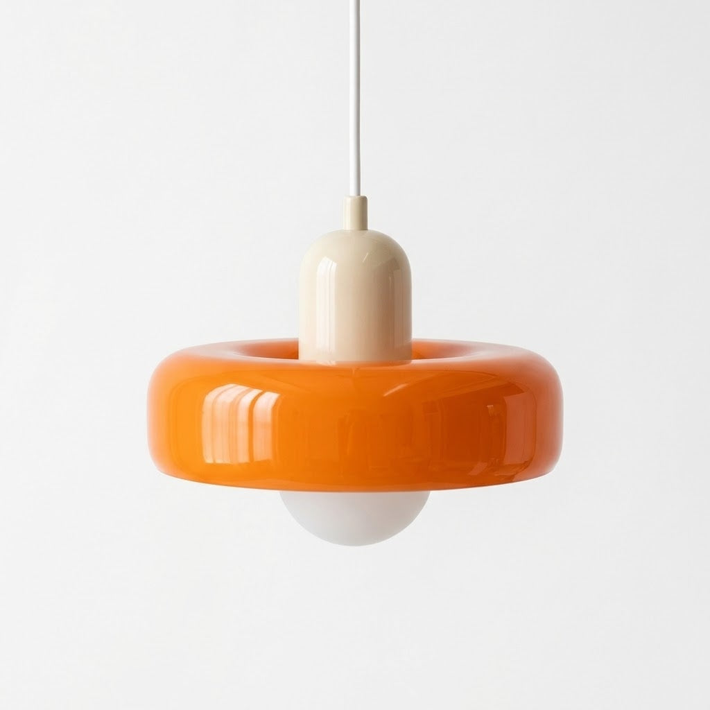 A modern pendant light with a glossy orange ring-shaped shade, a cream-colored central neck, and a white globe bulb below, suspended by a thin white cord against a plain white background.