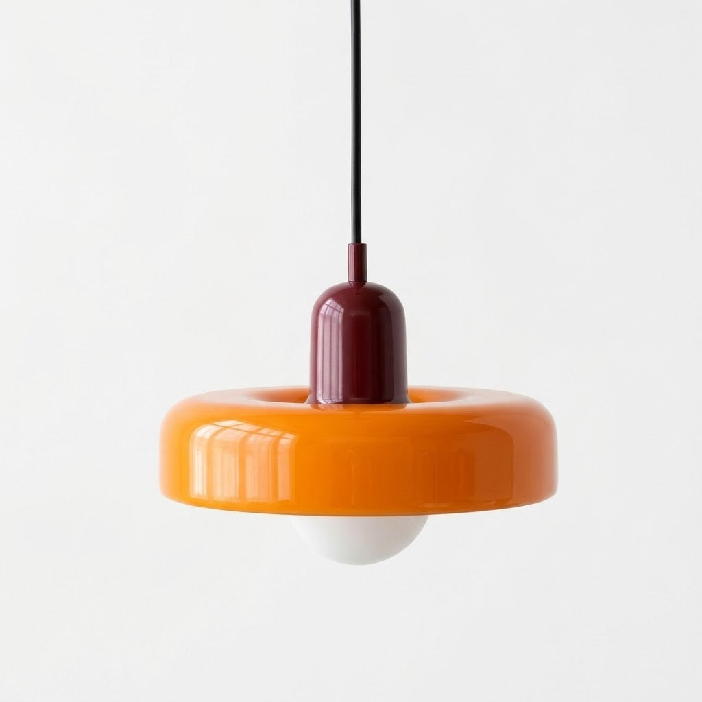 A modern pendant light with a glossy orange ring-shaped shade, a dark red central collar, a black hanging cord, and a white globe bulb below, shown against a plain white background.