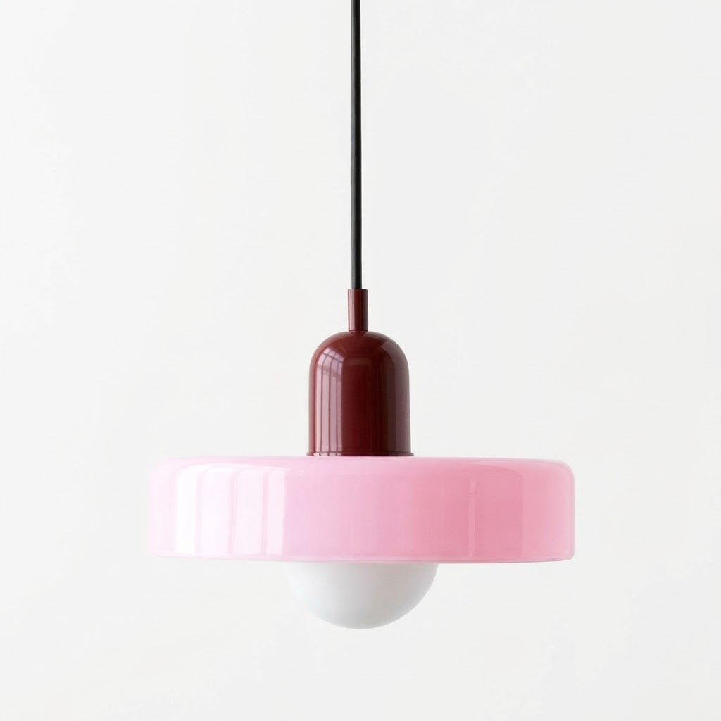 A modern pendant light with a wide pink flared shade, a dark red cylindrical neck, a black hanging cord, and a white globe bulb below, shown against a plain white background.