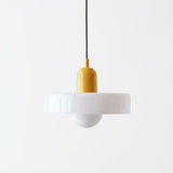 A modern pendant light with a wide white flared shade, a yellow cylindrical socket, and a black hanging cord, shown against a plain white background.