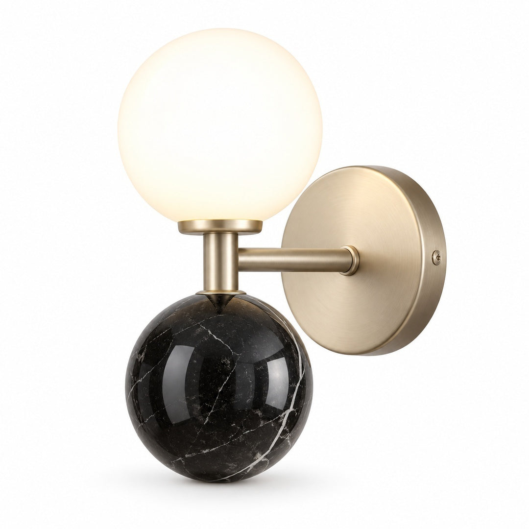 Modern wall sconce with a glowing frosted glass globe, a polished black marble sphere base, and a brushed brass wall mount on a white background.