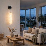 Black wall sconce with four glowing milky white globes on a pale living room wall near a sofa and wooden coffee table.