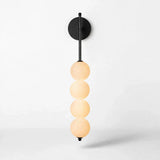 Black iron wall sconce with a round backplate and four vertically stacked milky white globes glowing warmly against a white background.