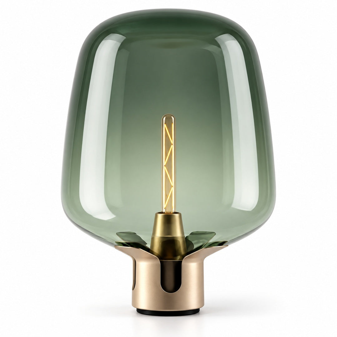 A modern table lamp with a translucent smoky green glass shade and a brushed brass metal base, featuring a visible warm-toned filament bulb inside, set against a plain white background.