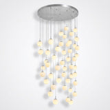 Modern multi-light chandelier with a circular brushed silver ceiling canopy and numerous hanging glass globes emitting a warm yellow glow, shown against a plain light gray wall.
