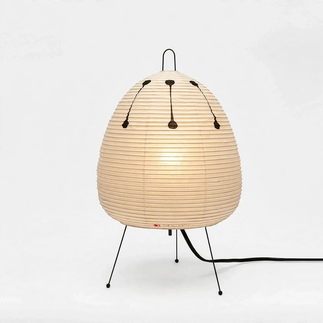 A modern table lamp with a ribbed, egg-shaped beige shade supported by three thin black metal legs, shown against a plain white background.