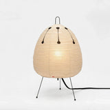A modern table lamp with a ribbed, egg-shaped beige shade supported by three thin black metal legs, shown against a plain white background.