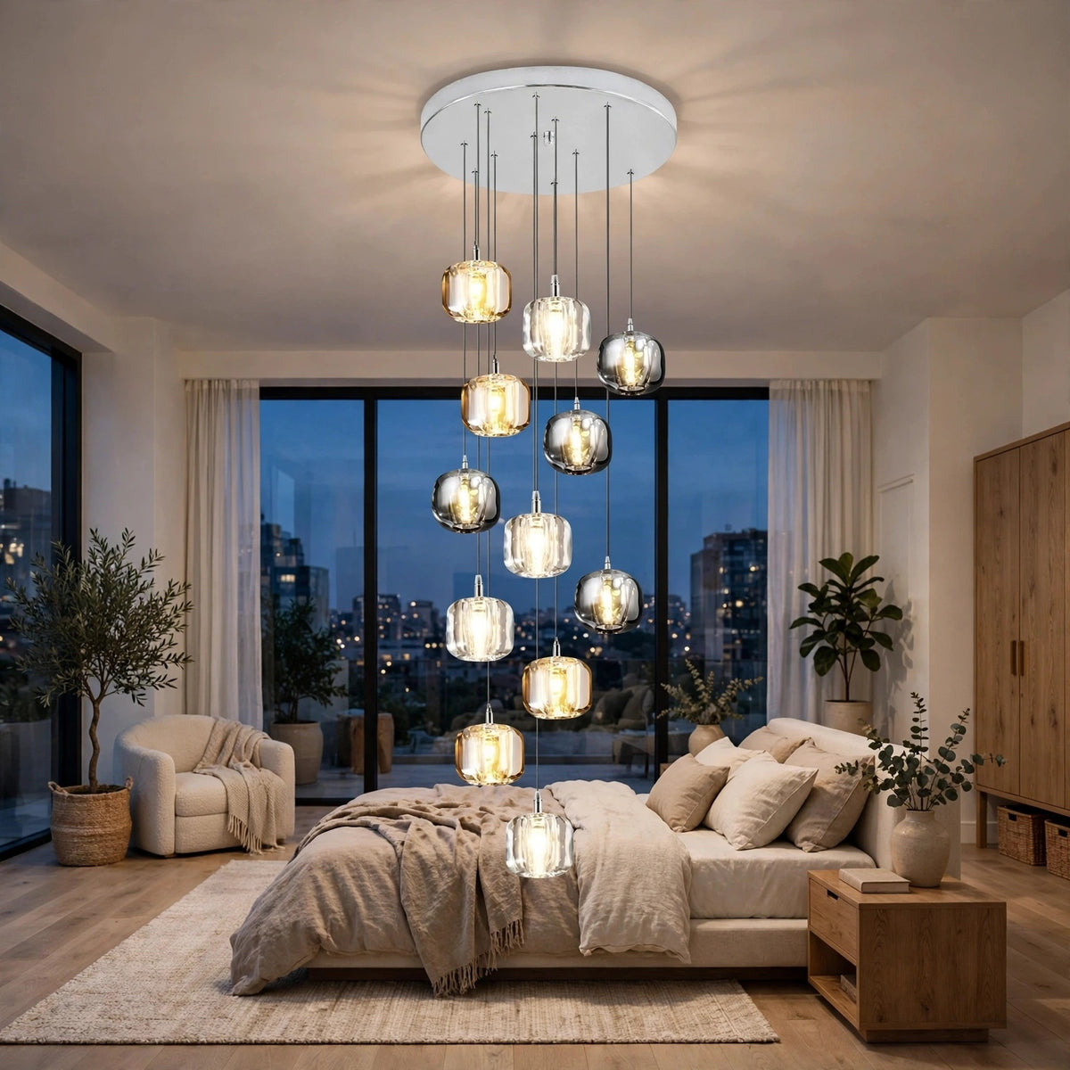 A modern multi-light chandelier with clear glass cylindrical and spherical pendant shades hangs over a bed in a contemporary bedroom with large windows, city views at dusk, beige bedding, and wood furniture.