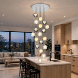 A modern multi-light pendant chandelier with clear glass spherical shades and warm white bulbs, hanging over a kitchen island in a bright, contemporary apartment interior.