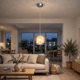 A single-light amber crystal chandelier glows in a living room with a beige sofa, wooden coffee table, and potted tree.