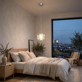 A single-light clear crystal chandelier hangs above a beige bed beside a large window overlooking city lights at dusk.