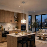 A single-light clear crystal chandelier illuminates a white kitchen island surrounded by wooden cabinetry and large windows at dusk.