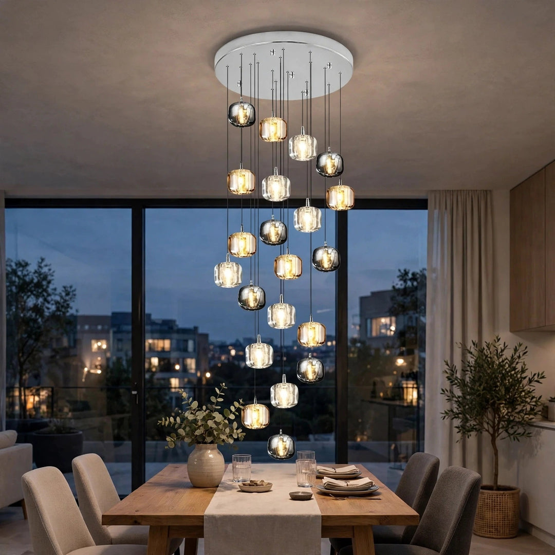 A modern multi-light chandelier with clear glass and metallic spherical bulbs hangs over a dining table in a contemporary dining room at dusk.
