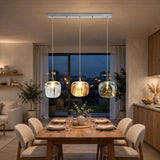 A modern 3-light linear ceiling pendant chandelier with clear glass globes and warm glowing bulbs, hanging over a wooden dining table in a contemporary dining room.