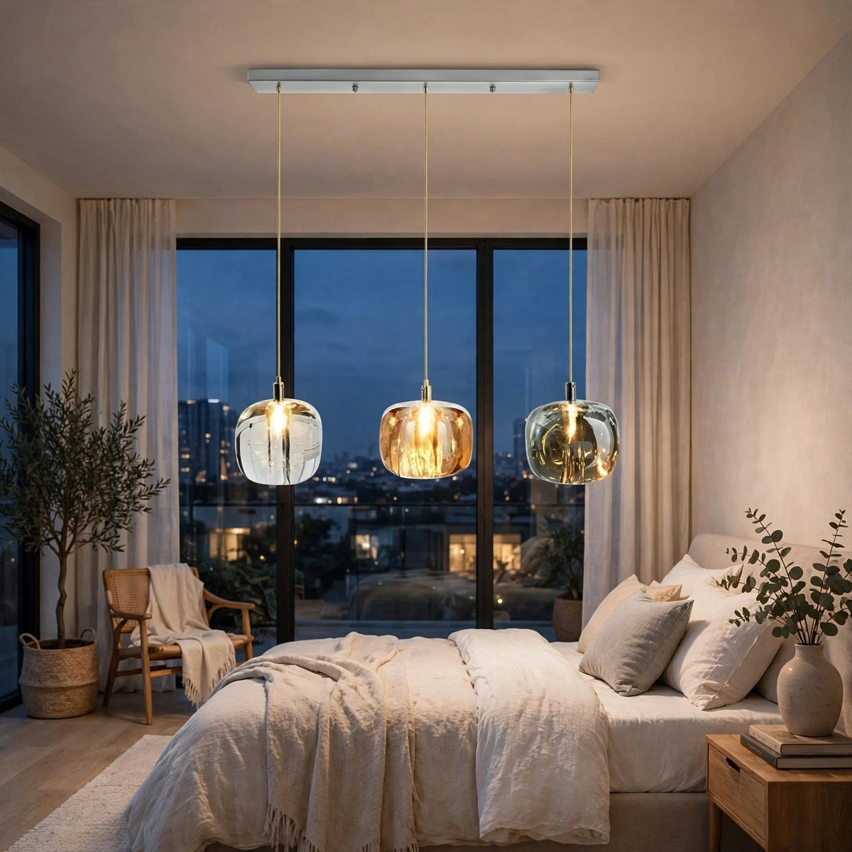 Linear chandelier with three clear, amber, and smoky crystal shades hangs above a white bed beside large windows overlooking the city at dusk.