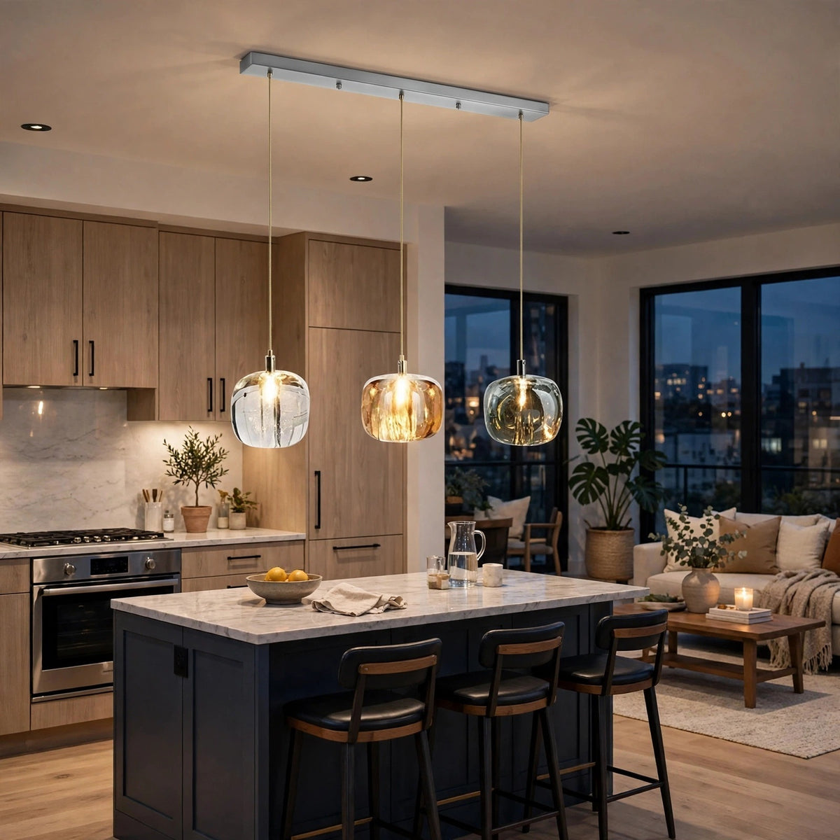 A modern three-light linear pendant chandelier with clear and amber glass globes hanging over a kitchen island in a contemporary apartment interior.