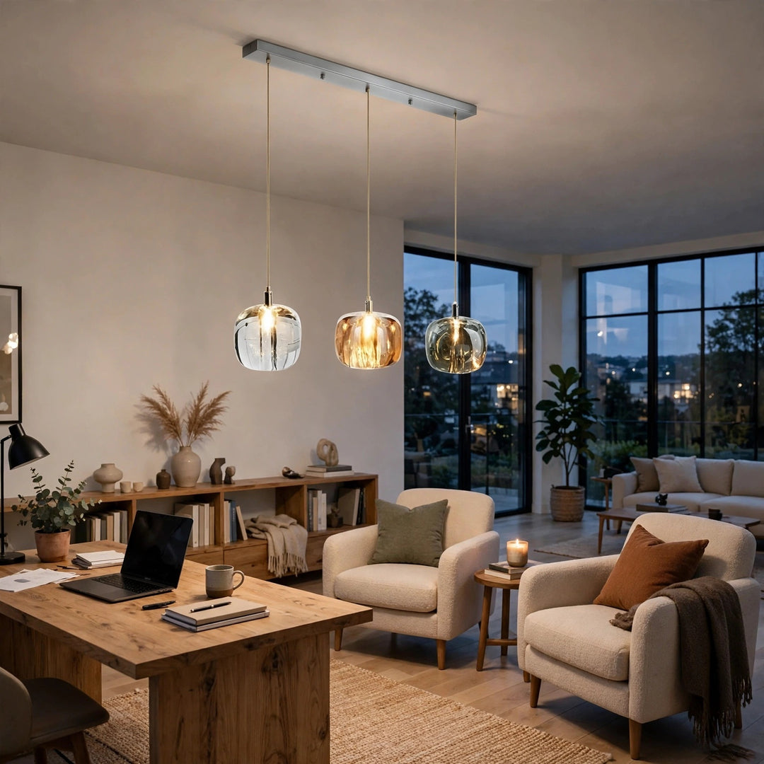 A three-light linear chandelier with clear, amber, and smoky grey crystal shades hangs above a wooden desk in a furnished living room.