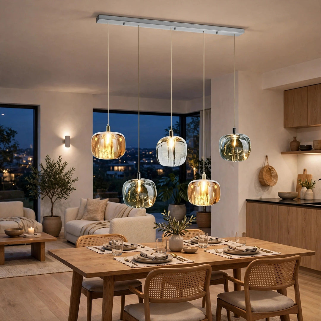 A five-light linear chandelier with amber, clear, and smoky crystal shades hangs above a wooden dining table with woven-back chairs.