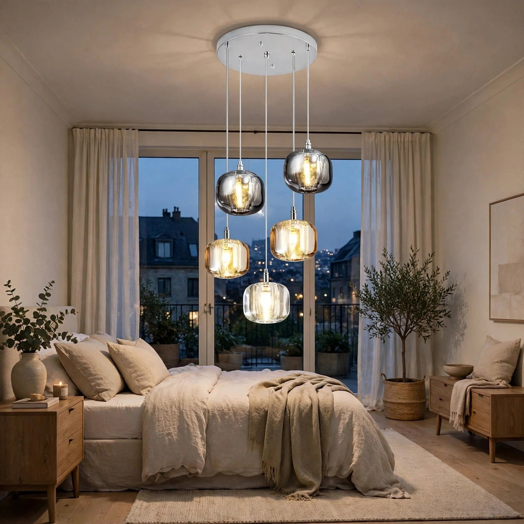 A modern multi-light pendant chandelier with five smoky glass shades hangs over a neatly made bed in a softly lit bedroom.
