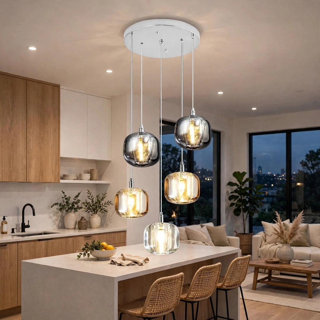 A modern 5-light linear pendant chandelier with clear glass and brushed silver metallic shades hanging over a kitchen island in a contemporary living space.