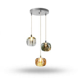 A chandelier has three illuminated clear, smoky grey, and amber shades at staggered heights beneath a round silver canopy against white.