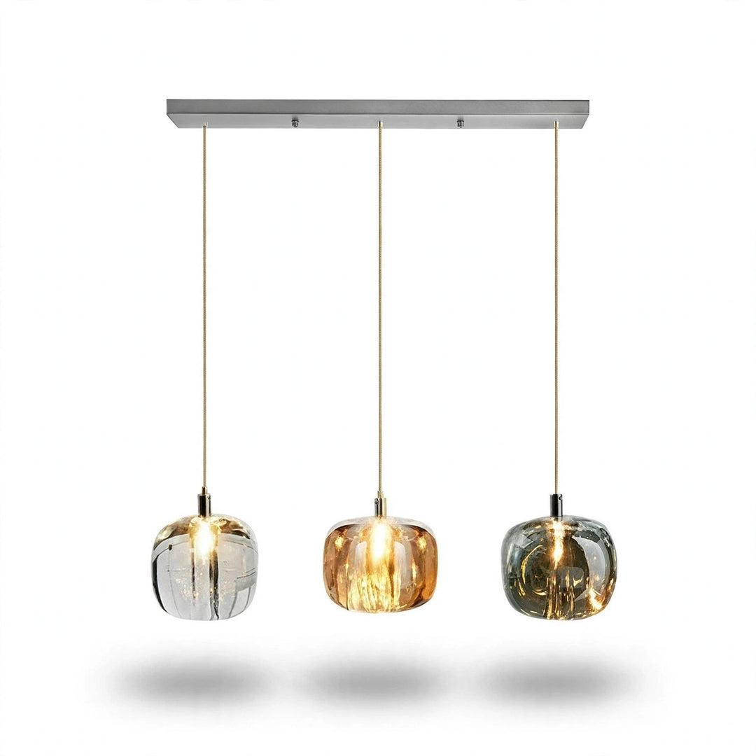 A linear chandelier has three illuminated clear, amber, and smoky grey shades in an even row beneath a rectangular silver canopy against white.