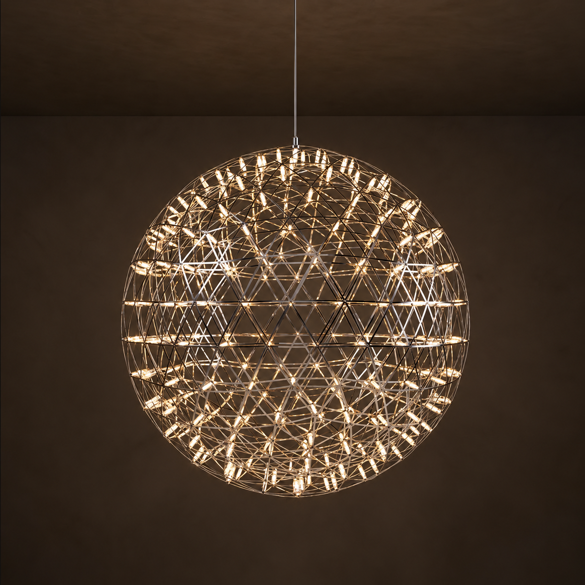 A spherical geometric wire chandelier pendant light with many small illuminated bulbs, hanging from a thin cord against a dark brown wall and ceiling.