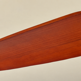 Ceiling fan light blade shown close up, with reddish-brown wood grain and a curved edge against a beige background.