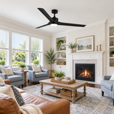 A modern black ceiling fan with a light fixture is shown installed in a bright, styled living room with a fireplace, blue armchairs, a wooden coffee table, and a patterned rug.